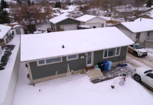 Aerial view of a snow-covered house in a residential area with cars parked outside.