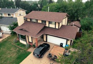Aerial view of a two-story house with a brown roof, driveway, and a parked SUV.