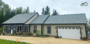 A single-story house with dark siding, a white garage door, and a landscaped front yard.